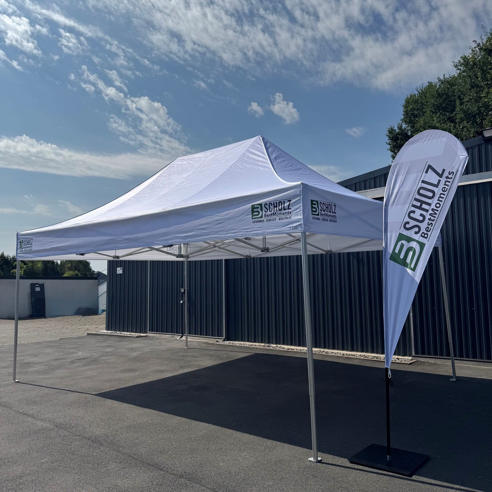 Flexzelt Pro-Tent 500 in Schrägansicht auf einem Hof, daneben eine Beachflag von Scholz BestMoments