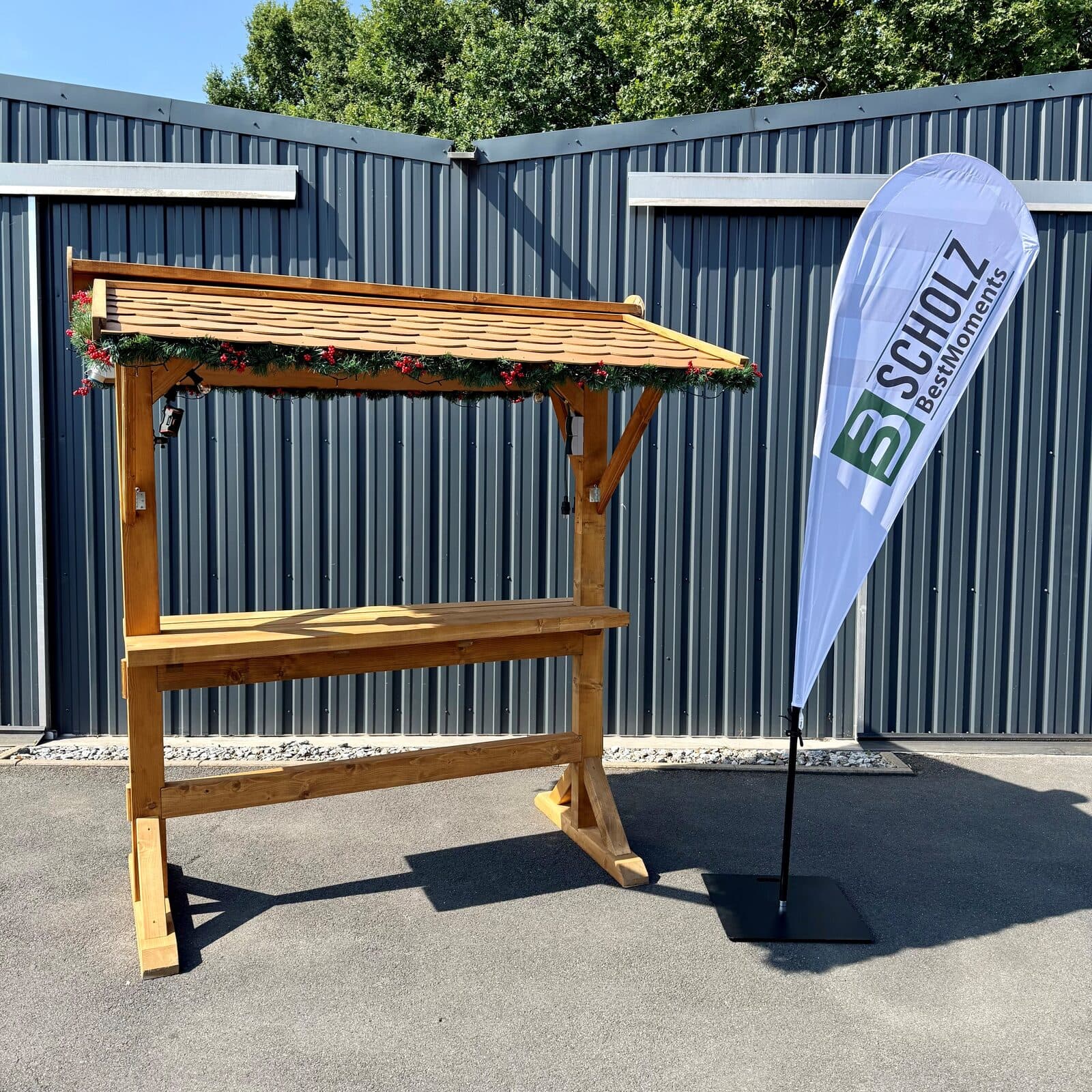 Seitenansicht des überdachten Holz-Stehtisches mit Schindeldach und Tannengirlande